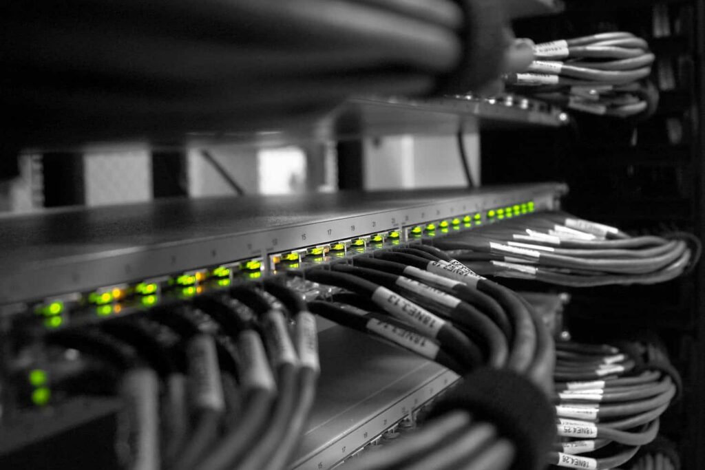 Bastidor de rede com switch iluminado e cabos de rede organizados e etiquetados num armário técnico