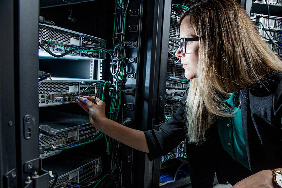 A female IT technician in a data centre plugs a network cable into a rack-mounted server.
