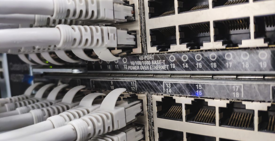 Nahaufnahme eines Netzwerk-Patchpanels mit mehreren RJ-45-Ethernet-Anschlüssen und eingesteckten grauen Kabeln in einem Serverschrank, die die Datenverkabelung zeigen.