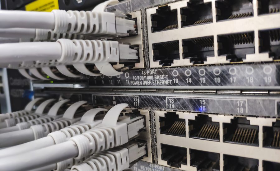 Gros plan sur un panneau de raccordement réseau comportant plusieurs ports Ethernet RJ-45 et des câbles gris branchés sur ceux-ci dans une armoire à serveurs, illustrant le câblage de données.